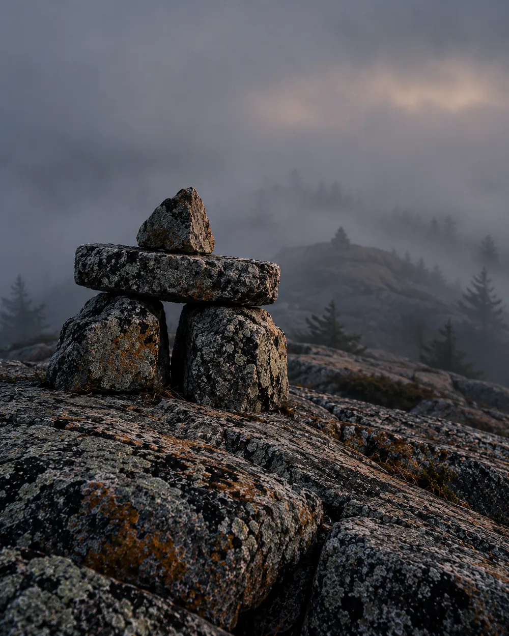A stone trail-marker cairn on a granite summit in fog