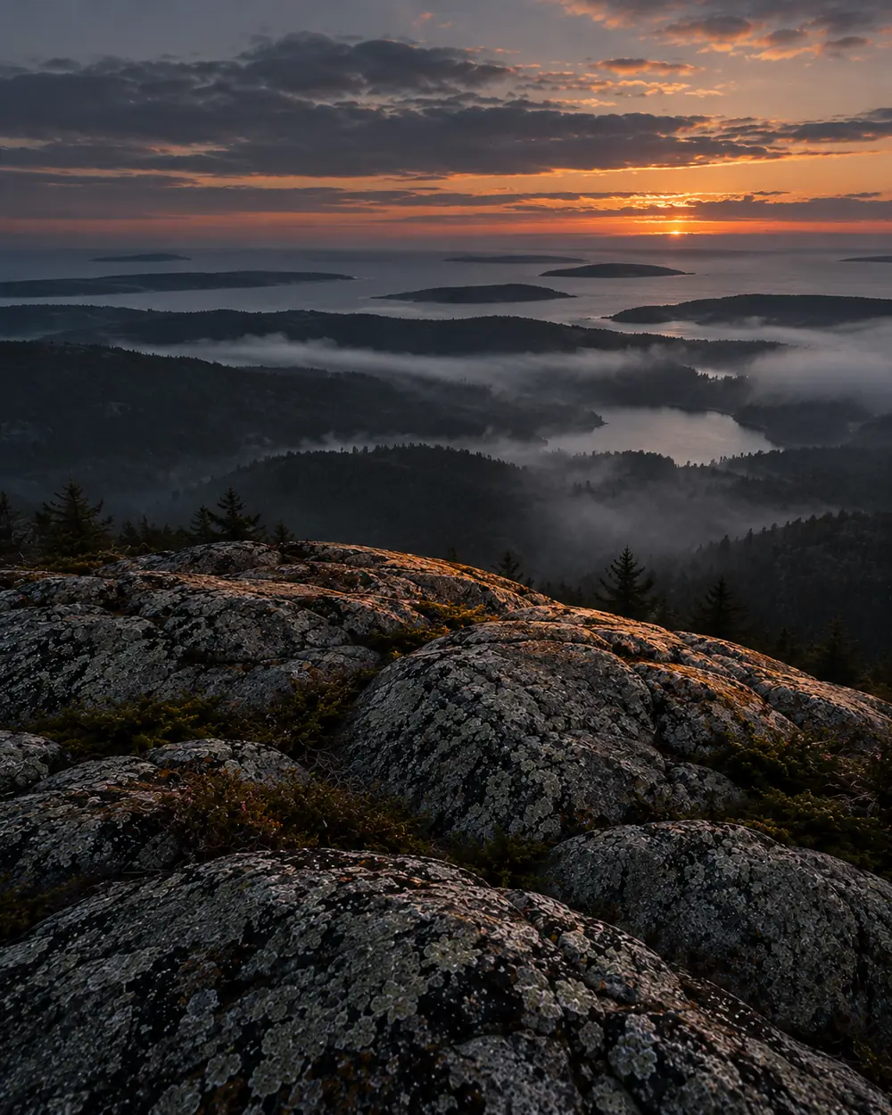 First light over a granite summit, with islands and low fog below